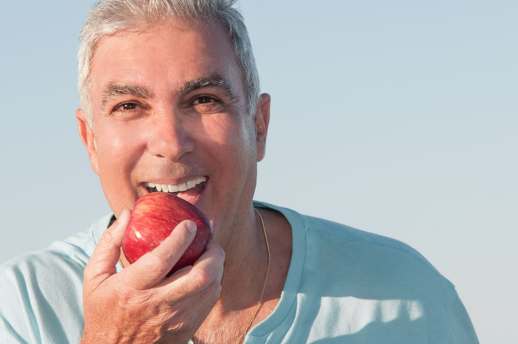 A man happily eating an apple after an oral surgery. A man with dentures enjoying an apple. A man with dental implants enjoying an apple.